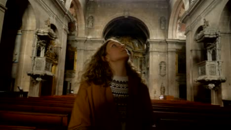 tourist girl inspects catholic church inside, circling around with head raised