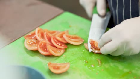 close up of a cook's hands with white latex gloves, cutting red juicy tomatoes with a professional knife, on a green plastic cutting board