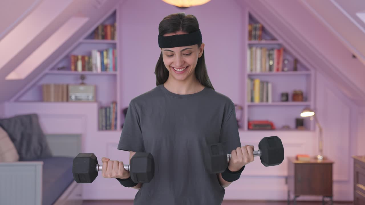 행복 한 인도인 여자 가 무거운 덤벨 을 들어 올리고 있다