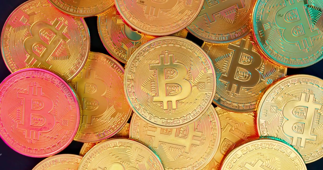 Pila di monete di criptovaluta Bitcoin dorate con riflessi colorati.