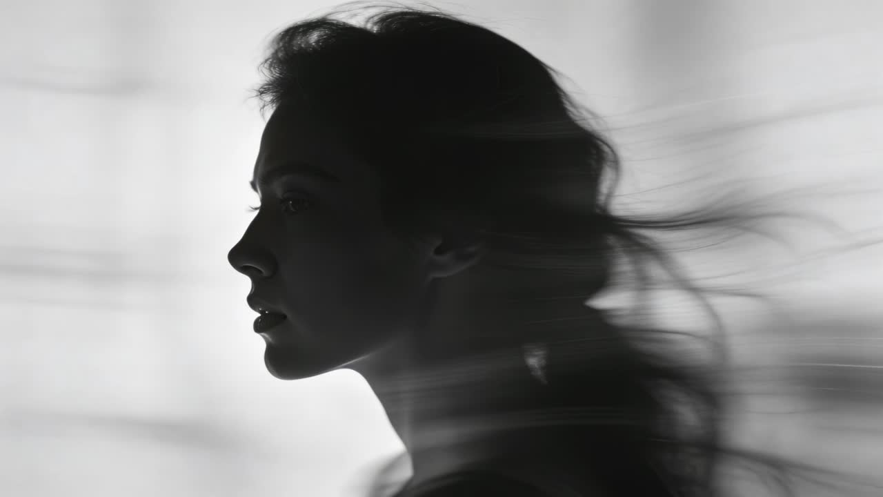 Facing right woman wearing thin strap top in backlit studio, fan pushing ponytail making silhouette