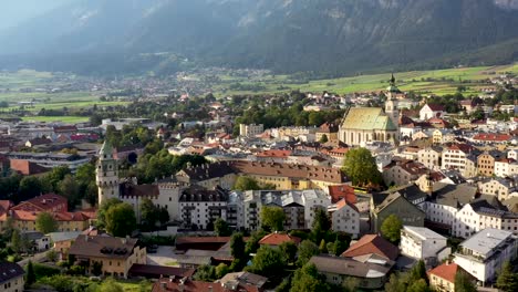 Vista-Aérea-De-La-Ciudad-Montañosa-De-Austria-Con-Iglesias,-Casas-Coloridas,-Torre,-Paisaje-Otoñal-Al-Atardecer,-Río-Alpes-Austriacos-Desde-Arriba,-Austria,-Europa