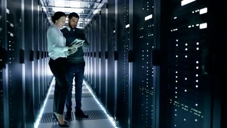 técnicos de servidores masculinos y femeninos que trabajan en un centro de datos. ejecutando diagnósticos de servidores de rack. la mujer usa una tableta.