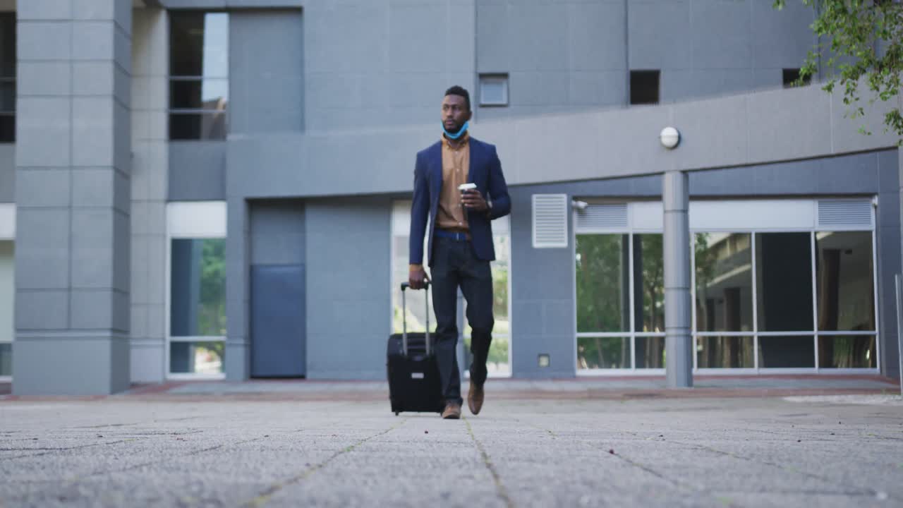 African american businessman with face mask walking with suitcase