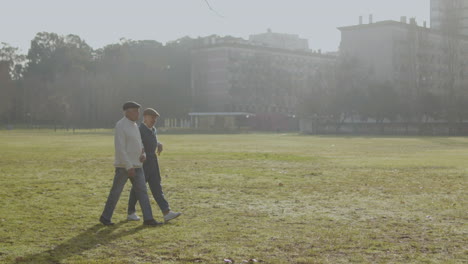 älteres-Ehepaar,-Das-An-Warmen-Herbsttagen-Im-Stadtpark-Spazieren-Geht,-Mit-Mehrstöckigen-Gebäuden-Im-Hintergrund