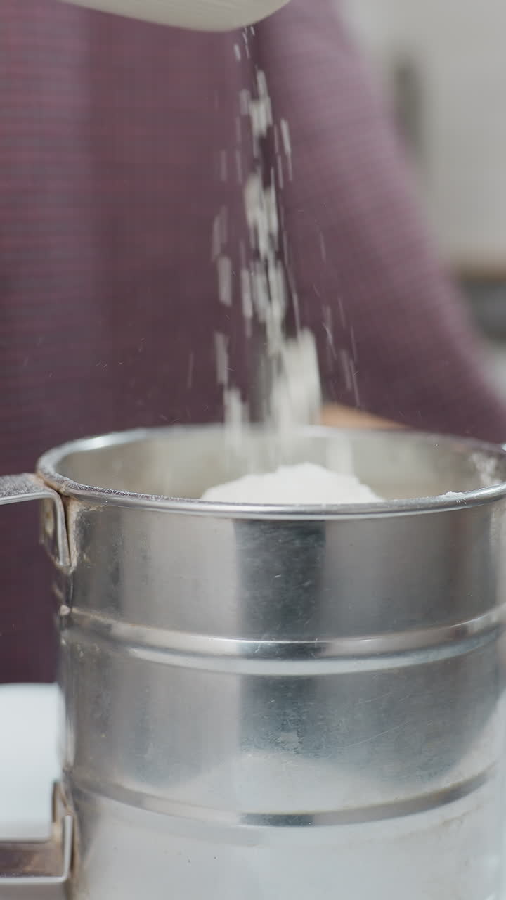 primer plano de leche que se vierte en una taza de acero inoxidable colocada en un plato de plástico blanco, encimera de la cocina con un cuenco y un batidor en el fondo