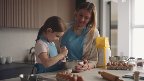 loving mother is teaching her little daughter to cook cake mom and child are spending time together in kitchen