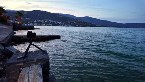 camera set up near the water at dusk with a view of agios nikolaos in the background