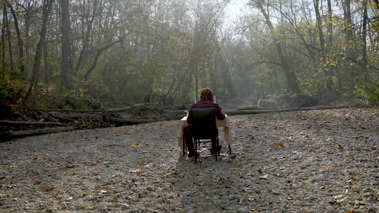 tiro de seguimiento hacia el hombre sentado solo en medio del bosque místico, luces matutinas a través de los árboles, conceptual
