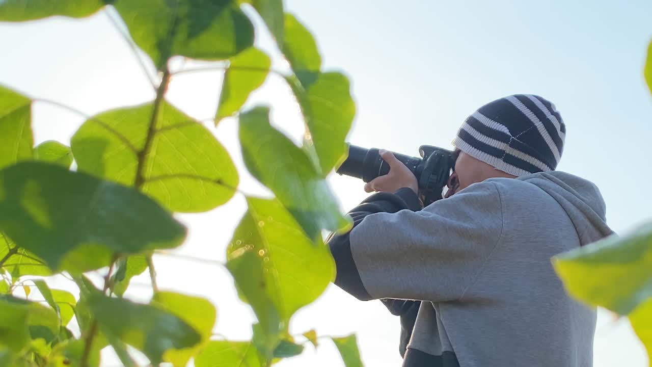fotógrafo tomando fotos con cámara dslr en el parque, hoja en primer plano, soleado