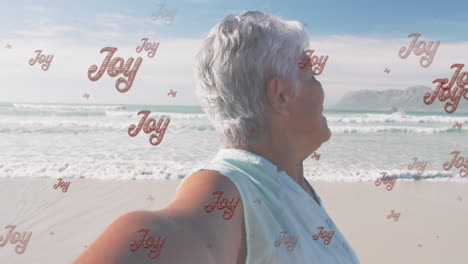 animación de saludos de navidad texto sobre mujer biracial senior en la playa.