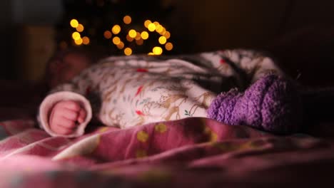 Niña-Sonriente-Acostada-En-Una-Cama-Y-Durmiendo-Frente-A-Un-árbol-Decorado-De-Navidad