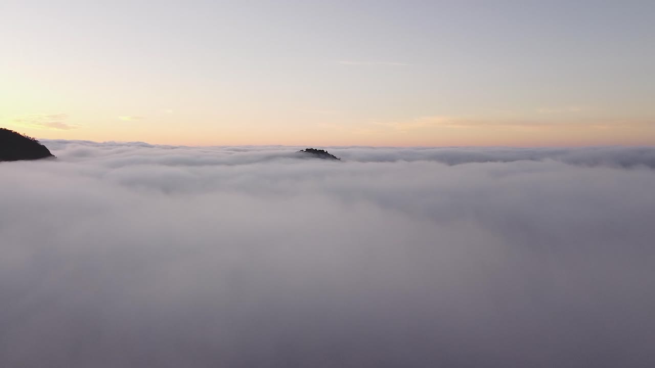 drone vuela sobre una capa de nubes donde sobresale la cima de una montaña durante un amanecer