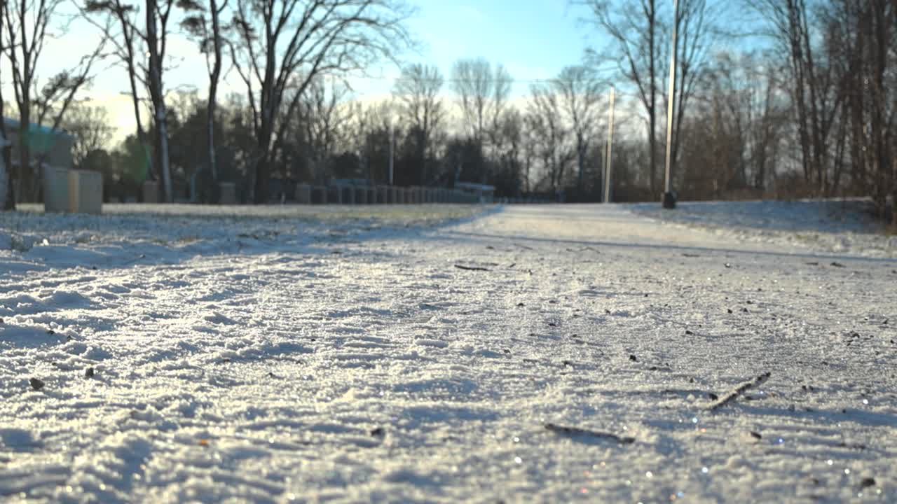 은 날 동안 겨울에 눈이 인 도로 또는 보행자 보행자 도로를 가로질러 미끄러지는 영상 또는 카메라, 태양이 바닥에 있는 가지와 자갈에서 그림자를 만들어내는 동안.