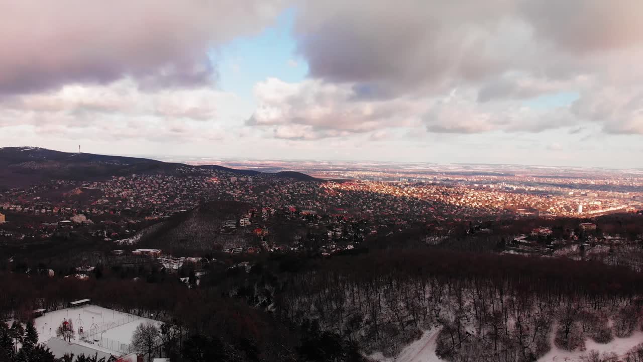 Winter aerial pan above a scenery forest with a town between the snowy hills in Europe