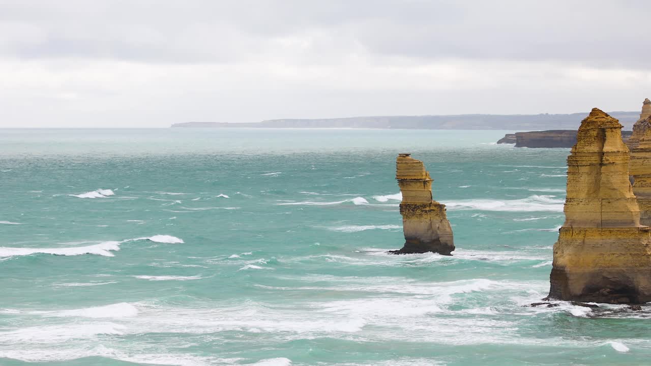Dynamic coastal scene of the Twelve Apostles with turquoise waves under overcast skies at Port Campbell, Australia