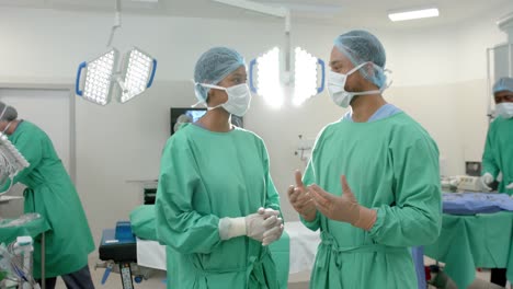 portrait of diverse surgeons wearing surgical gowns, talking in operating theatre, slow motion