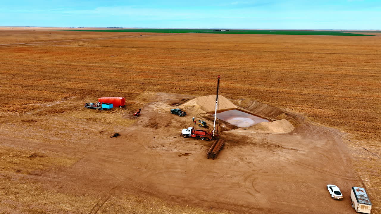 Approaching the site for producing the natural resources. A truck with set rig tower and pile of metal pipes are at the location. Aerial view.
