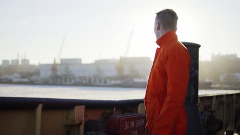 harbor worker in orange uniform standing by the board of the ship. lens flare. slow motion