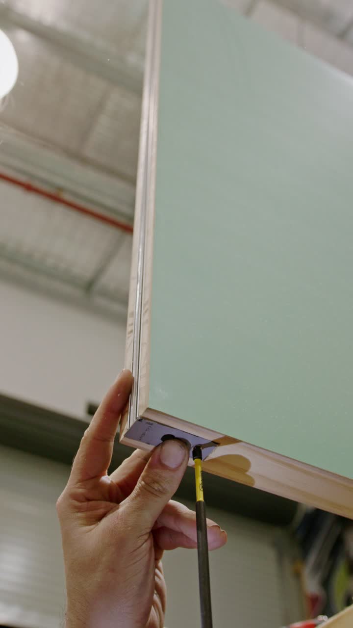 Primo piano, ripresa verticale di un artigiano che fissa una staffa angolare metallica alla parte inferiore di un mobile laminato o di un pannello di porta usando un cacciavite.
