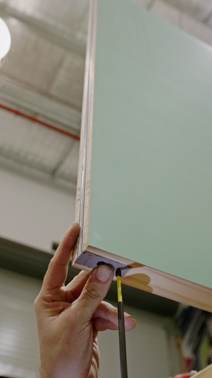 Primo piano, ripresa verticale di un artigiano che fissa una staffa angolare metallica alla parte inferiore di un mobile laminato o di un pannello di porta usando un cacciavite.