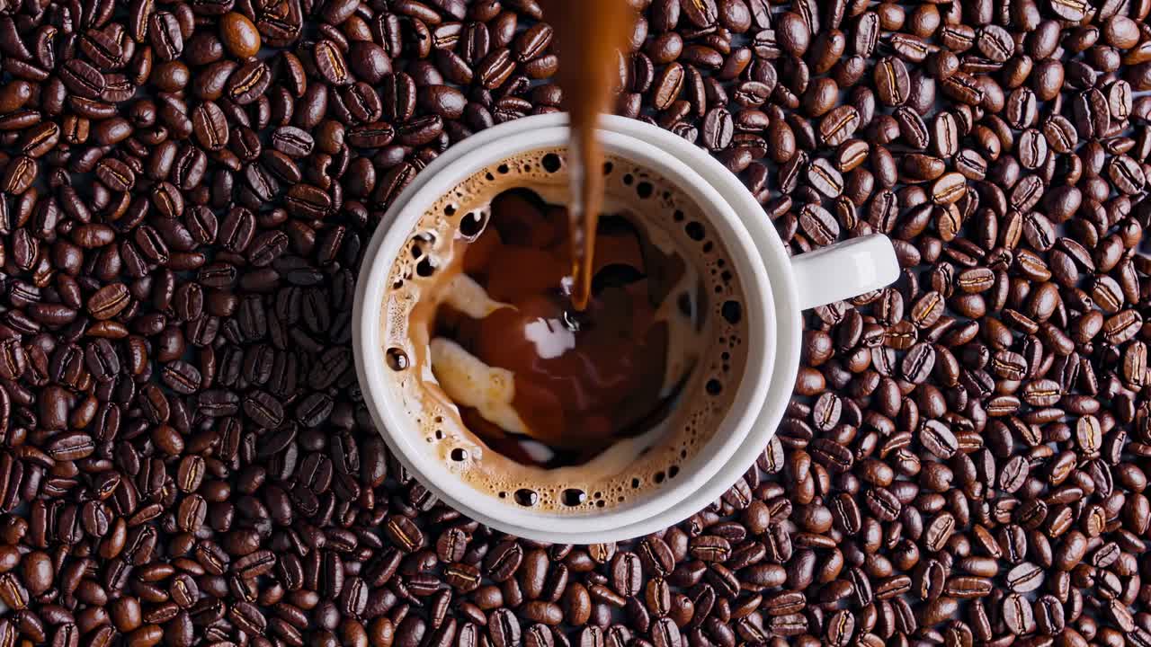 Top-down video shot of coffee pouring into a cup surrounded by beans, emphasizing rich textures