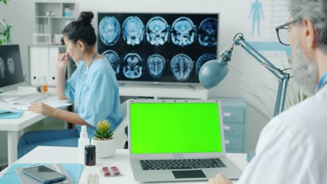 médico usando una computadora portátil de pantalla verde mientras la enfermera escribe registros médicos en el hospital