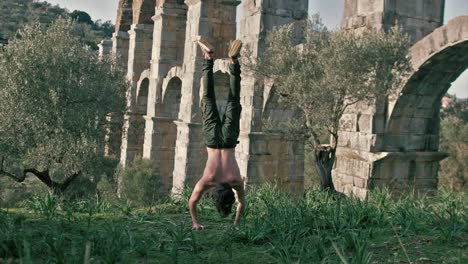 Young-man-performs-one-handstand-push-up-outdoors-in-front-of-ancient-aqueduct