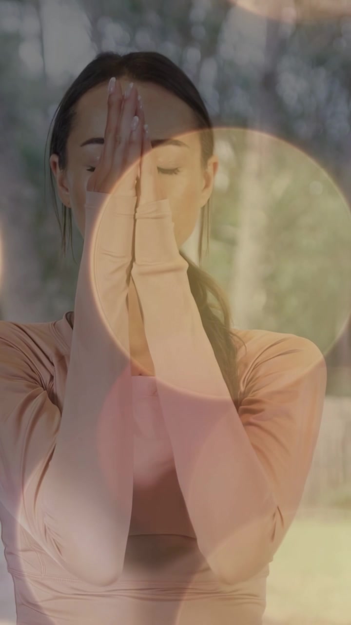 Video vertical: Mujer respirando y moviendo los brazos en postura de oración a la altura del pecho para el bienestar, mientras el efecto bokeh flota.