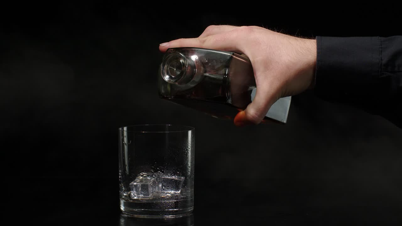 hombre vertiendo whisky en un vaso con cubos de hielo