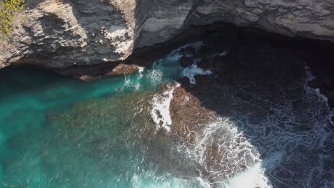 Vista-Aérea-Del-Agua-Azul-Cristalina-De-La-Bahía-Rota-En-Nusa-Penida,-Indonesia-Con-Las-Olas-Golpeando-Los-Acantilados