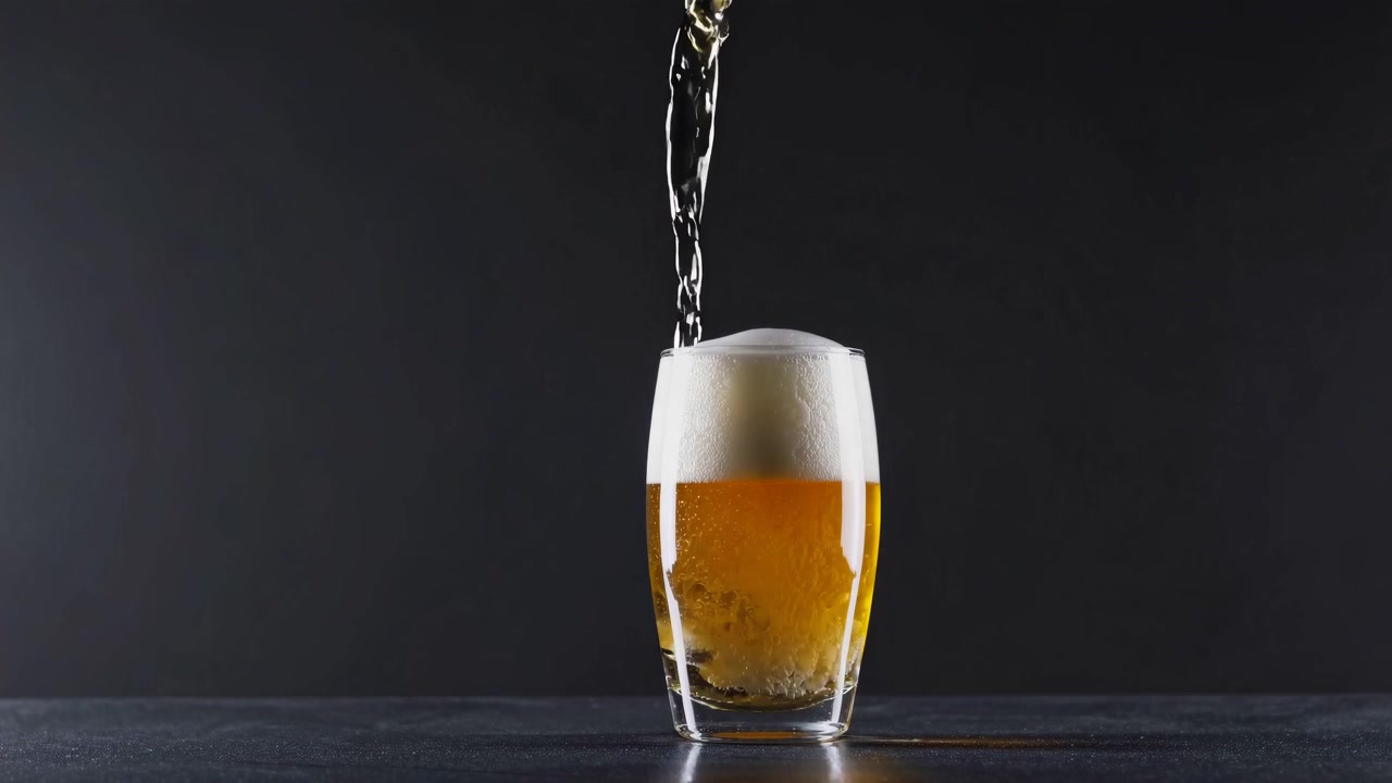 Birra dorata versata dalla bottiglia nel bicchiere con schiuma bianca