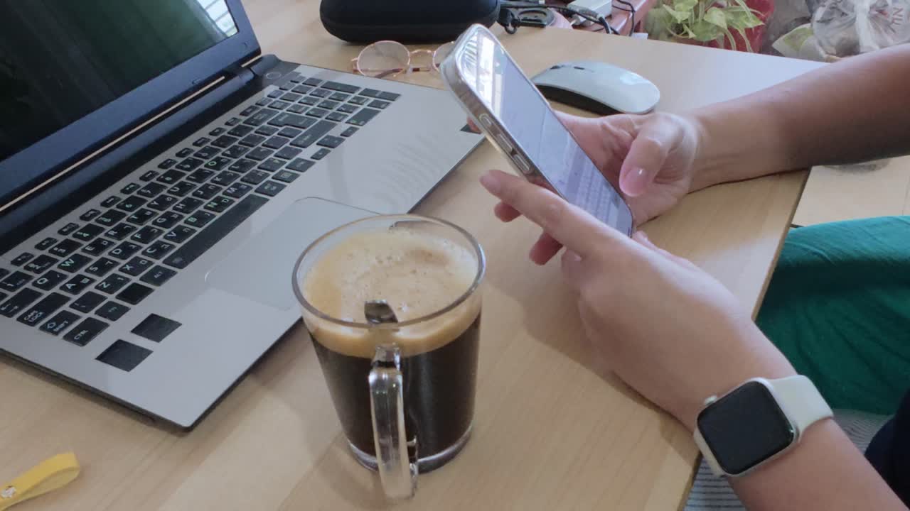 Starting the workday: person with coffee, phone, and laptop at desk.