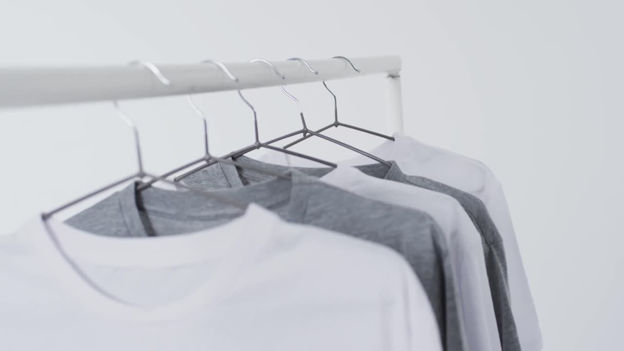 Video of white and grey t shirts on hangers and copy space on white background