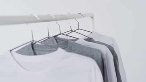 video of white and grey t shirts on hangers and copy space on white background