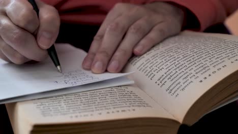 a student reads a book and takes notes with a pen