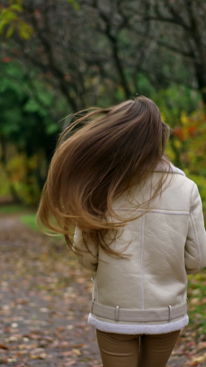 Attractive smiling girl running slowly in the autumn park. Brunette runs and her long hair moving beautifully. Blurred nature backdrop.