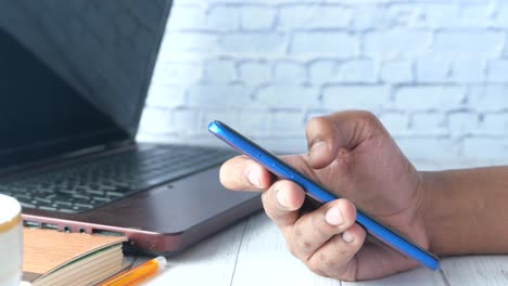 person using smartphone next to a laptop