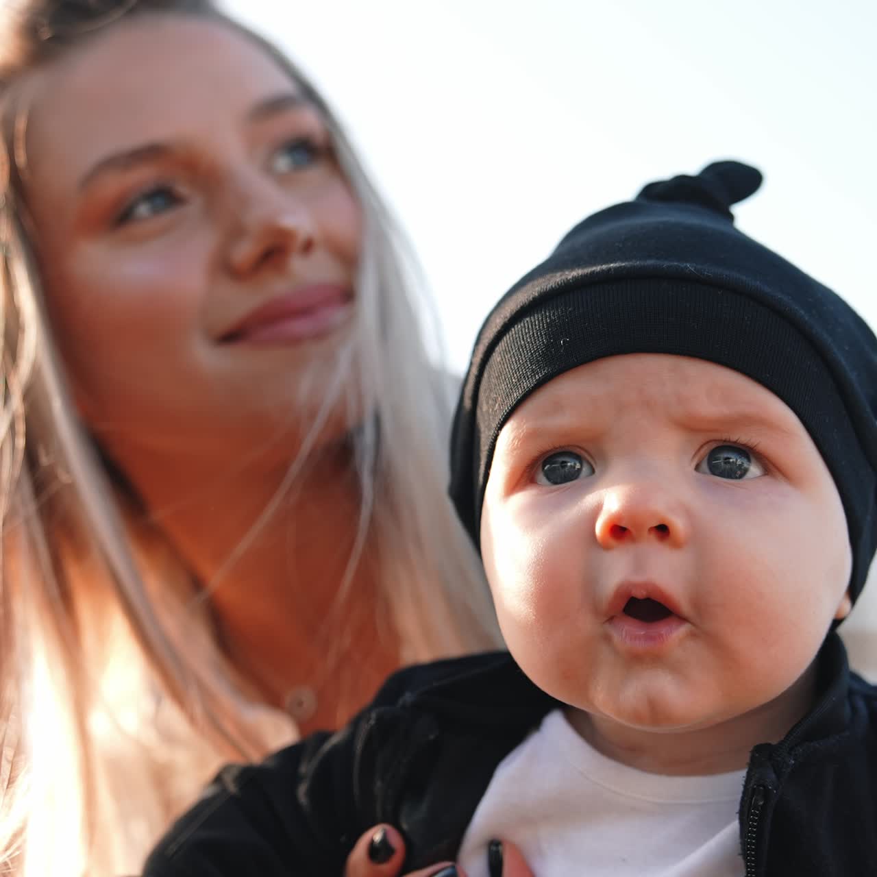 Ein wunderschönes Baby mit schwarzer Mütze und Jacke. Die Mutter hält ihren kleinen Sohn vor die Kamera. Nahaufnahme. Vertikaler Bildschirm
