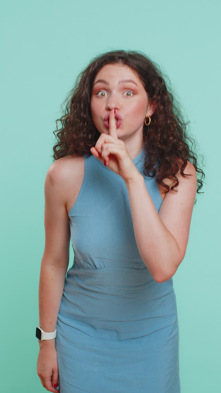 Young woman presses finger to lips makes silence gesture sign do not tells secret stop gossip