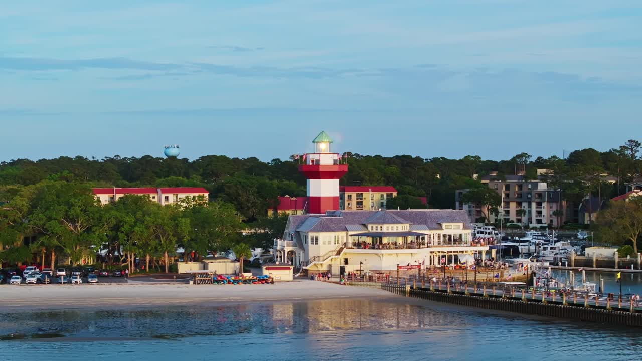Harbour Town Pier South Carolina USA, marina inlet with golden sunny weather across lighthouse, aerial establishing
