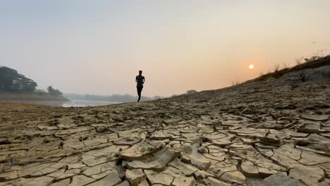 wide shot of active runner man jogging in countryside dry land, foggy sunrise in winter morning