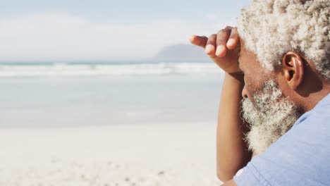 Senior-african-american-man-sitting-and-looking-away-on-sunny-beach