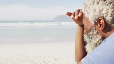 senior african american man sitting and looking away on sunny beach