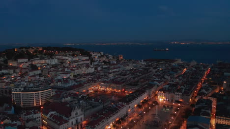 Aerial-night-view-of-urban-city-center-of-Lisbon-with-rows-of-traditional-modern-houses,-castle-on-the-hill-and-large-public-squares-with-lights