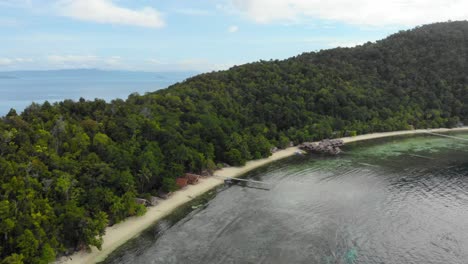 Muestra-Una-Foto-De-Casas-De-Huéspedes-A-Lo-Largo-De-Una-Playa-De-Arena-Frente-A-Un-Paisaje-Isleño-Cubierto-De-Espesa-Vegetación