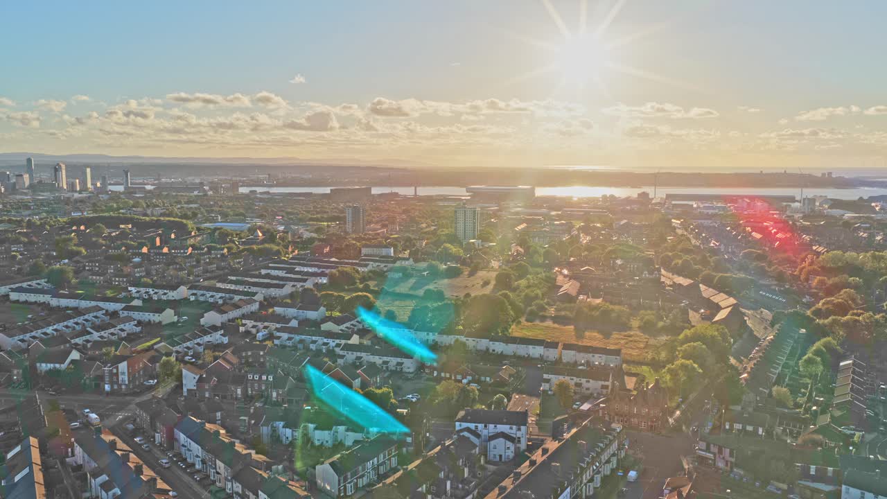 Cinematic aerial drone footage of the neighbourhood surrounding Liverpool FC’s iconic Anfield stadium, captured during sunset. The golden-hour light highlights residential streets, rows of houses