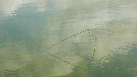 Surface-of-the-water,-reflection-of-the-clouds,-single-grass-sticking-out