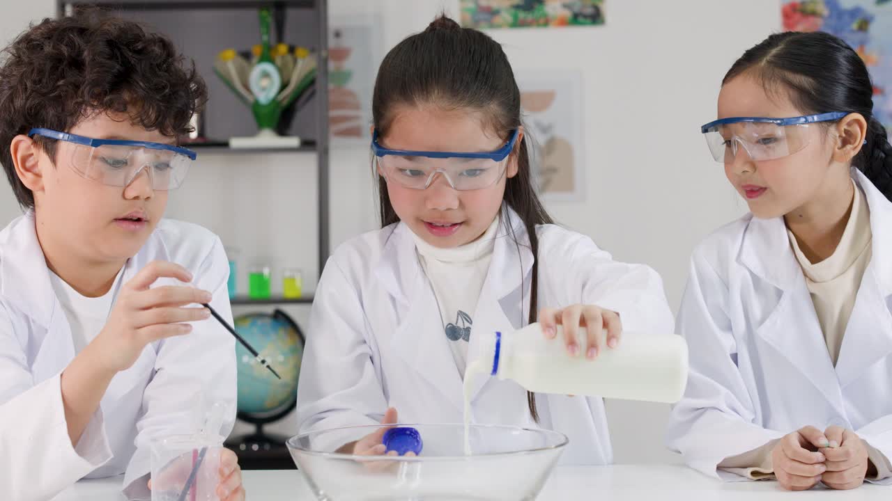 実験着とゴーグルを着用した3人のアジア人学生が、科学実験のためにボウルに牛乳を注いでいる。