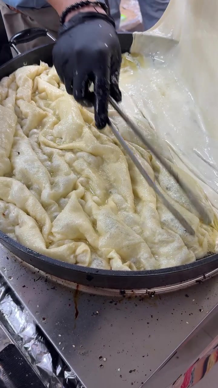 Vendedor de comida callejera cocinando pan plano tradicional en sartén grande